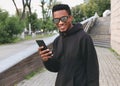 Portrait smiling african man with phone looking at camera wearing black hoodie, sunglasses on city Royalty Free Stock Photo