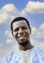 Portrait of a smiling African man wearing a boubou in the street, blue sky, white clouds, photo