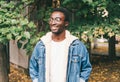 Portrait smiling african man wearing jeans jacket, eyeglasses in autumn city park Royalty Free Stock Photo