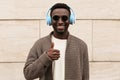 Portrait smiling african man in wireless headphones listening to music showing gesture thumbs up as like sign on city street Royalty Free Stock Photo