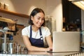 Portrait of smiling asian barista, cafe owner entrepreneur, working on laptop, processing orders on computer, standing Royalty Free Stock Photo