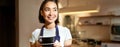 Portrait of smiling asian barista, girl in uniform, serving coffee, waitress holding cup of drink, working in cafe Royalty Free Stock Photo