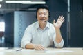 Portrait of a smiling Asian businessman talking on a video call in a headset, greeting the camera, sitting in the office Royalty Free Stock Photo
