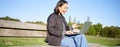 Portrait of smiling asian girl sits on bench in park, talks to friend online via laptop, video chats, using computer to Royalty Free Stock Photo