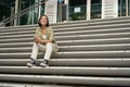 Portrait of smiling asian girl sits on stairs outdoors, sending message, using smartphone app, looking at mobile phone Royalty Free Stock Photo