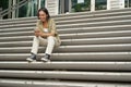 Portrait of smiling asian girl sits on stairs outdoors, sending message, using smartphone app, looking at mobile phone Royalty Free Stock Photo