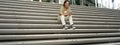 Portrait of smiling asian girl sits on stairs outdoors, sending message, using smartphone app, looking at mobile phone Royalty Free Stock Photo