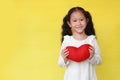 Portrait of smiling asian kid girl holding a red heart for you isolated on yellow background with copy space Royalty Free Stock Photo
