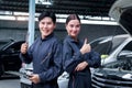 Portrait of smiling Asian mechanic man and beautiful woman in uniform standing and give thump up at garage vehicle shop, auto Royalty Free Stock Photo