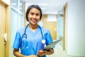 Portrait of smiling asian nurse or female doctor health worker wearing blue uniform holding digital tablet while posing on modern Royalty Free Stock Photo