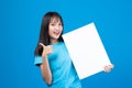 Portrait of smiling asian woman holding empty blank board on blue studio background. Happy young girl standing with white square Royalty Free Stock Photo