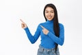 Portrait of smiling asian woman pointing fingers left, showing amazing news, promo banner, offer, standing over white Royalty Free Stock Photo