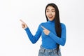 Portrait of smiling asian woman pointing fingers left, showing amazing news, promo banner, offer, standing over white Royalty Free Stock Photo