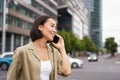 Portrait of smiling asian woman talking on mobile phone, walking on street near busy road and speaking to friend Royalty Free Stock Photo