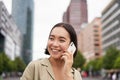 Portrait of smiling asian woman talking on mobile phone, walking on street near busy road and speaking to friend Royalty Free Stock Photo