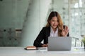 Portrait of smiling asian woman waving hello talking on video call. Successful young woman sitting white suits. Business