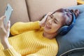 Portrait of a smiling Asian woman wearing a pair of headphones and using her phone and listening to music while sitting Royalty Free Stock Photo