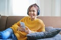 Portrait of a smiling Asian woman wearing a pair of headphones and using her phone and listening to music while sitting Royalty Free Stock Photo