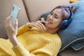 Portrait of a smiling Asian woman wearing a pair of headphones and using her phone and listening to music while sitting Royalty Free Stock Photo