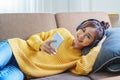 Portrait of a smiling Asian woman wearing a pair of headphones and using her phone and listening to music while sitting Royalty Free Stock Photo