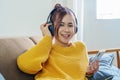Portrait of a smiling Asian woman wearing a pair of headphones and using her phone and listening to music while sitting Royalty Free Stock Photo