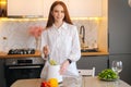 Portrait of smiling attractive young woman making healthy vegetable detox smoothie juice in blender standing posing in Royalty Free Stock Photo