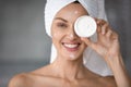 Smiling young woman using moisturizing face cream in bathroom Royalty Free Stock Photo