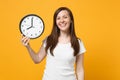 Portrait of smiling attractive young woman in white casual clothes holding in hand round clock isolated on bright yellow