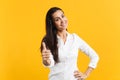 Portrait of smiling attractive young woman in white casual shirt looking camera, showing thumb up isolated on yellow Royalty Free Stock Photo