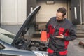 portrait of smiling auto mechanic with bottle of motor oil at car repair station