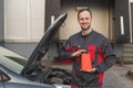 portrait of smiling auto mechanic with bottle of motor oil at car repair station.