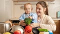 Portrait of smiling baby boy with young mother sitting on kitchen table and holding dish ingredients Royalty Free Stock Photo