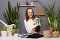 Portrait of smiling beautiful woman gardener working in her greenhouse or flower store, holding plant with soil, replanting Royalty Free Stock Photo