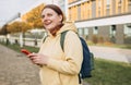 A portrait of a smiling beautiful woman texting sms with her phone on urban background. Happy student with backpack is Royalty Free Stock Photo