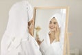 Portrait of smiling beautiful woman who after shower applies moisturizer on face.