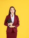 Portrait of smiling beautiful working woman in red dress holding diary  on yellow background Royalty Free Stock Photo