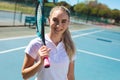 Portrait of smiling beautiful young caucasian female tennis player standing with racket at court Royalty Free Stock Photo