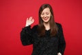 Portrait of smiling beautiful young woman in black fur sweater looking down waving hand isolated on bright red wall Royalty Free Stock Photo