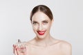 Portrait of smiling beautiful young woman holding showing perfume bottle in her hand, enjoying its smell and looking at camera, Royalty Free Stock Photo