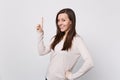 Portrait of smiling beautiful young woman in light clothes standing pointing index finger up on white wall Royalty Free Stock Photo