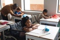 Portrait of smiling biracial elementary schoolgirl sitting on wheelchair at desk in classroom Royalty Free Stock Photo