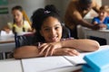 Portrait of smiling biracial elementary schoolgirl sitting on wheelchair at desk in classroom Royalty Free Stock Photo