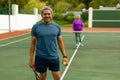 Portrait of smiling biracial senior man holding racket and ball playing tennis with wife at court Royalty Free Stock Photo