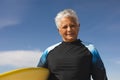 Portrait of smiling biracial senior woman carrying surfboard at beach against blue sky on sunny day Royalty Free Stock Photo