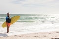 Portrait of smiling biracial senior woman holding surfboard on shore at sunny beach against sky Royalty Free Stock Photo