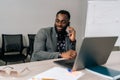 Portrait of smiling black businessman in suit using laptop talking on smartphone sitting at office desk. Happy confident Royalty Free Stock Photo