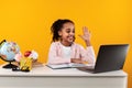 Portrait of smiling black girl sitting at table waving hand Royalty Free Stock Photo