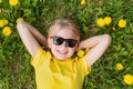 Portrait of smiling blond boy wearing sunglasses and yellow T-shirt lying on field of dandelions. Top view Royalty Free Stock Photo