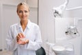 Portrait of smiling blonde female orthodontist doctor in white coat holding human jaws layout model with metal dental