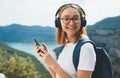 Portrait smiling blonde girl with hipser glasses and backpack connection cellphone device and listens music for headphones via wir Royalty Free Stock Photo